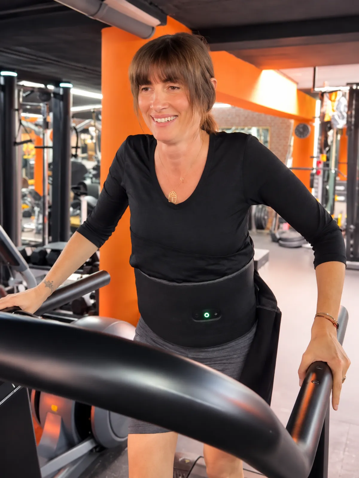 Une adhérente souriante porte la ceinture Slim Sonic pendant sa séance de cardio, au centre Platinium Training
