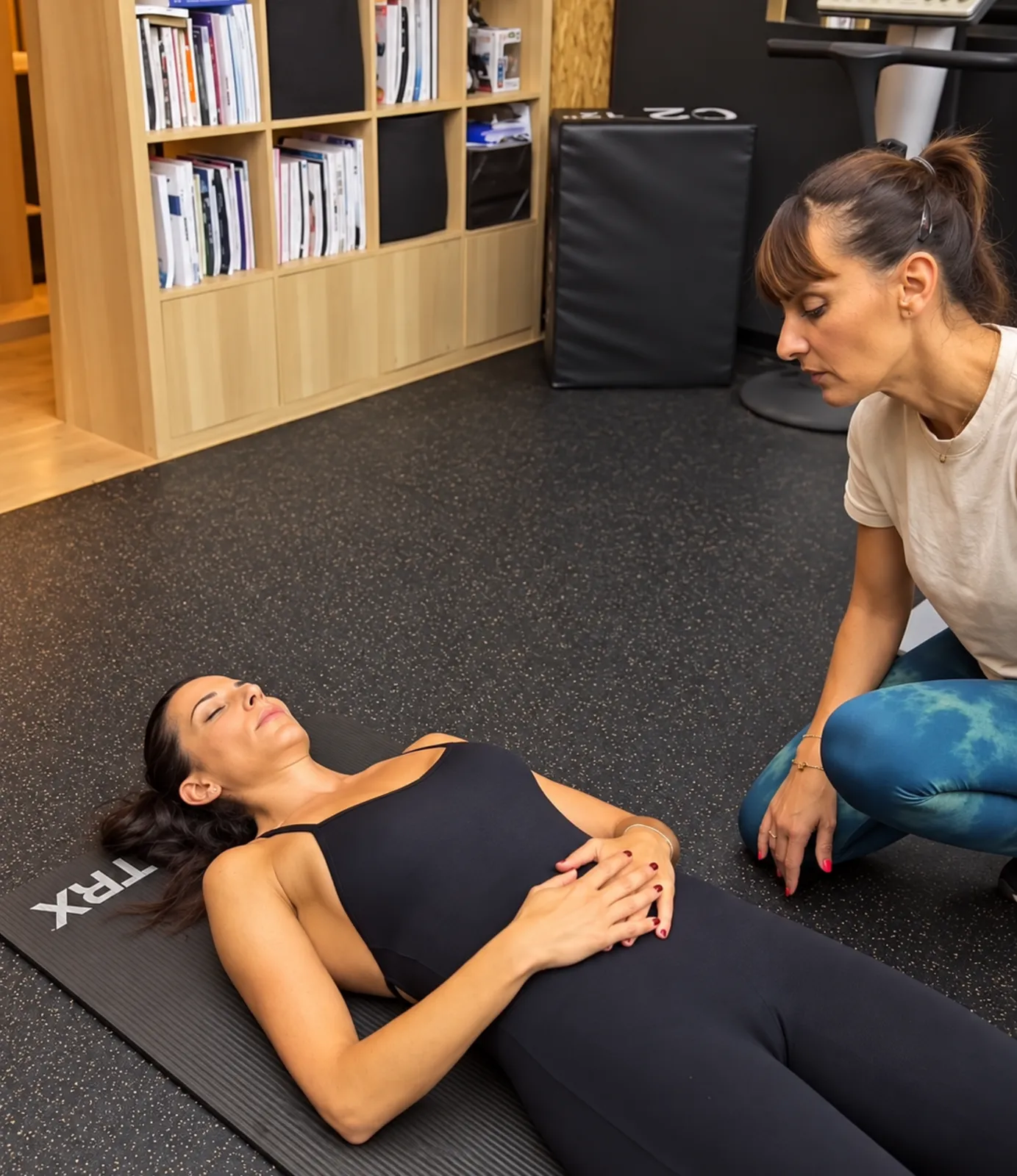 Une adhérente allongée sur un tapis respire calmement, guidée par sa coach, au centre Platinium Training