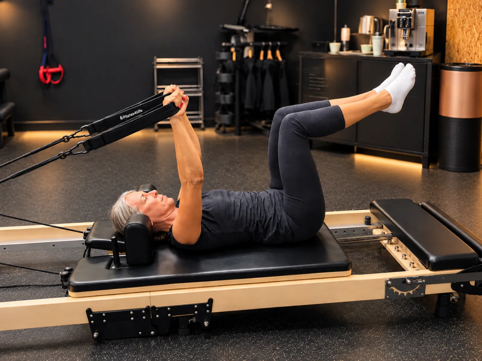 Une adhérente allongée sur le Pilates Reformer, jambes levées et sangles en main, au centre Platinium Training