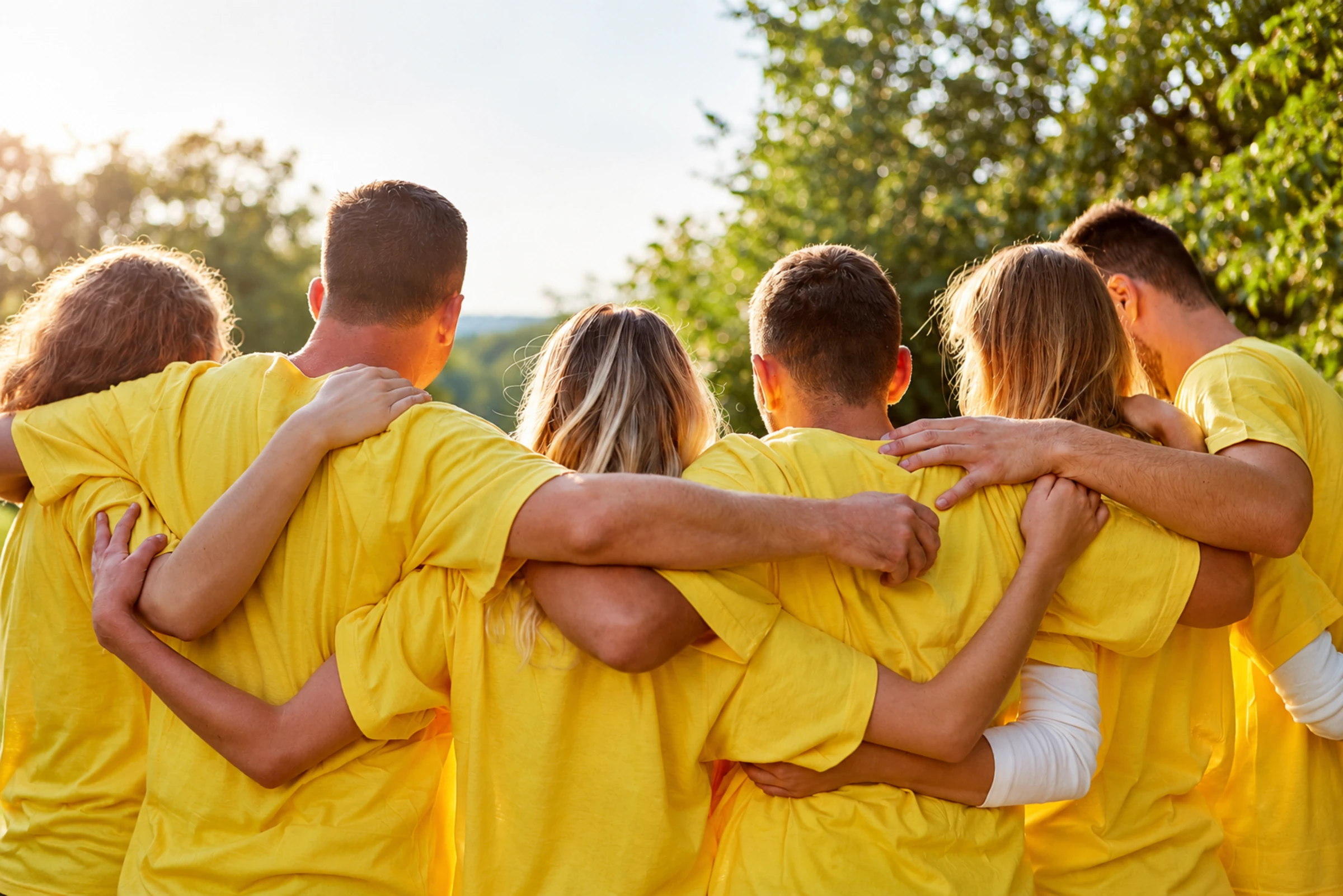 Une équipe en t-shirts jaunes se tient par les épaules, en plein air, après un défi collectif